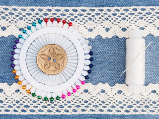 Beige lace, thread, needle, pins on jeans background. Sewing still life