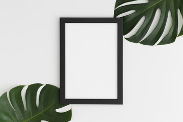 Top view of a black frame mockup with monstera leaf decoration. Portrait orientation.