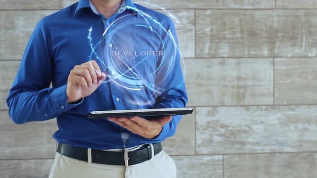 Man activates a conceptual hologram with text Developer. The guy in the blue shirt and light trousers with a holographic screen gadget on the background of the wall