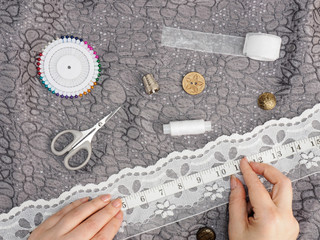 Woman measures white lace to sew to a dress of gray fabric