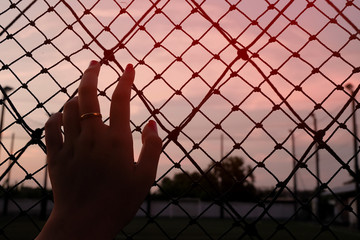 A lonely girl putting her hand on wire wall waiting for someone.