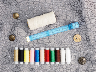 Tailor's tools - threads, tape measure, buttons on a background of gray fabric. Stitching still life