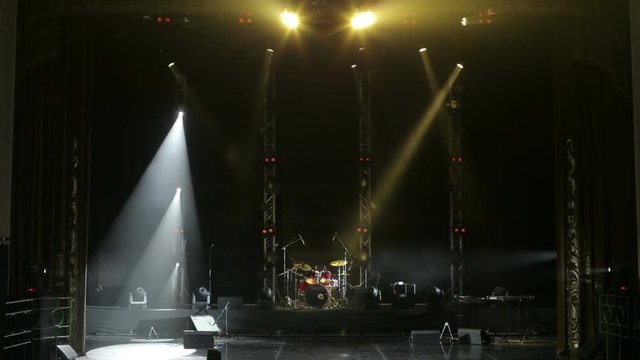 Colorful light flashing and white rays on an empty stage in the dark. Stage lighting. Light show. Musical equipment and lighting on the free scene. Musical instruments and drum set on an empty stage.