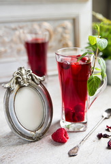 Red hibiscus tea in a transparent glass against the background of a vintage wall, with vintage frame and spoon. Copy space