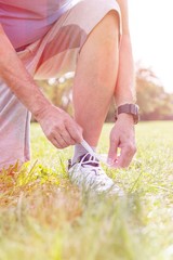 Low section of senior jogger tying shoelace on grassy field