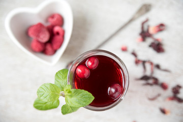 Red hibiscus tea in a beautiful cup, raspberries in a heart-shaped plate. Copy space