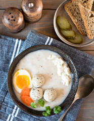 A plate with white Polish soup. White borsch with egg, meatballs, cottage cheese and carrots.
