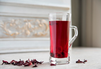 Red hibiscus tea in a transparent glass against the background of a vintage wall