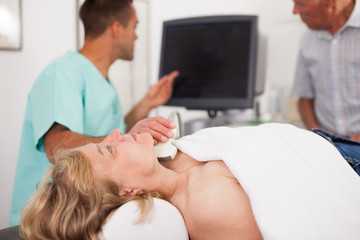 Obraz na płótnie Canvas Doctor conducting ultrasound examination of patient's thyroid lying