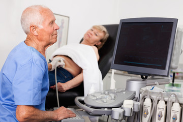 Mature male doctor using ultrasound scan examining female patient in modern hospital