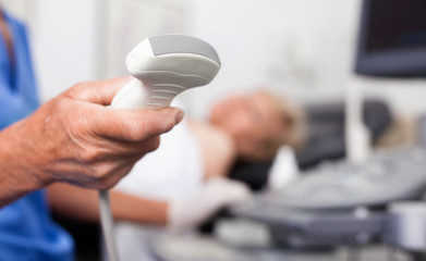 Male doctor holding ultrasonic probe in hand, ultrasound machine and patient ready for diagnostic