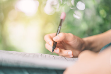 Woman hand using pen writing on paper  at coffee shop with nature green bokeh sun light abstract background.