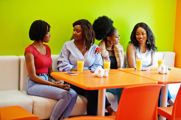Fototapeta na wymiar Four young african girls with juices sitting in bright colored fast food restaurant.