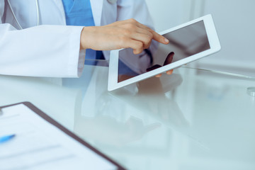 Female doctor using tablet computer while sitting at the workplace, close-up of hands. Medicine, healthcare and help concept