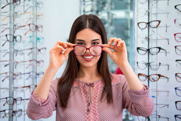 Health care, eyesight and vision concept - happy woman choosing glasses at optics store