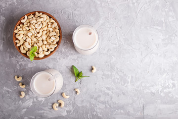 Organic non dairy cashew milk in glass and wooden plate with cashew nuts on a gray concrete background.