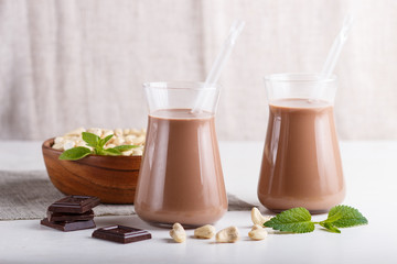 Organic non dairy cashew chocolate milk in glass and wooden plate with cashew nuts on a gray concrete background.