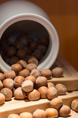 Hazelnut in shell poured from a white jug on wooden stand, brown orange background. Close-up, copy space, vertical layout