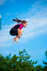 Little caucasian female 8 years old girl in neoprene shorty surfing wetsuit jumping from 5 mether...