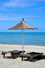 Umbrella and chaise lounges on the sandy beach. Wooden beach chairs, beds and straw umbrella on a tropical beach. Deck chairs and umbrella on a sandy beach. Summer holiday season concept
