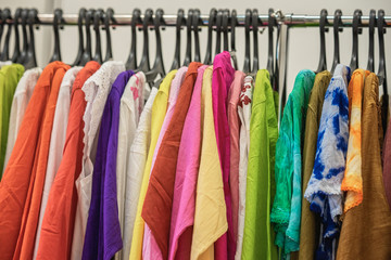 Colorful clothes on hangers for sale in shop. Summer season, assortment in a clothing store. Choice of cotton clothes of different colors on hangers