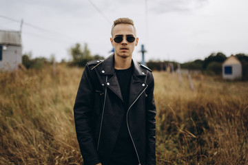 Young sexy man in leather jacket and sunglasses standing outdoor