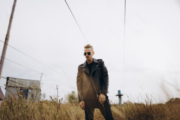 Young sexy man in leather jacket and sunglasses standing outdoor