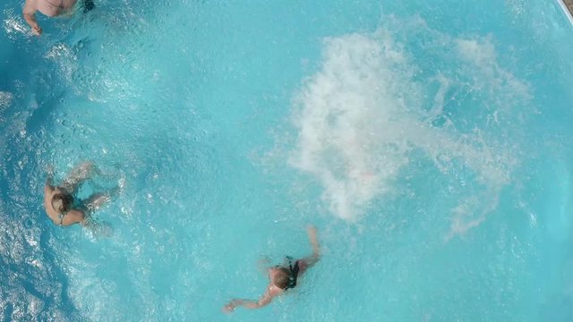 aerial shot of Company of friends having fun in swimming pool on sunny day. Girls swim in pool at time when men jump into water.