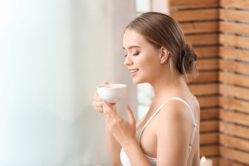 Beautiful young woman drinking coffee in spa salon