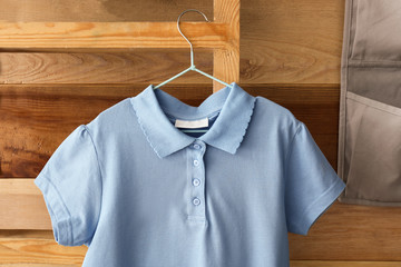 Stylish school uniform hanging on rack near wooden wall