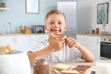 Funny little boy eating tasty toasts with chocolate spreading in kitchen © Pixel-Shot