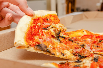 Female hand takes meat pizza with mushrooms from a simple cardboard box close up