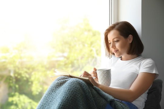 Morning Of Beautiful Young Woman Drinking Coffee While Writing In Notebook Near Window