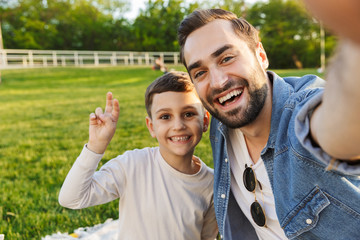 Young man having fun with his little brother or son outoors in park beautiful green grass take a...