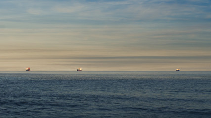 Obraz premium Evening sky horizon and sea. Three unidentifiable container ships outside La Spezia port, Liguria, Italy. Global trade background. Mediterranean.