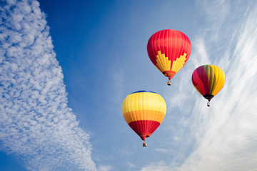 Colourful hot air balloons flying over white clouds and blue sky.