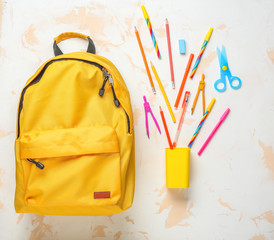 Backpack with school supplies on light background