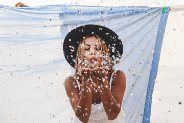 pretty woman with colorful straw hat blowing confetti