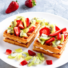 Belgian waffles with fruits strawberries and kiwi on white plate closeup. Tasty healthy breakfast