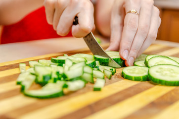 Female hand cuts cucumbers with a knife on the bars on a wooden plank close up