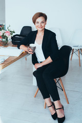 Young businesswoman sitting on the desk with with cup