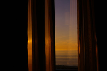 Sunset on the sea. View on seaside from the window with curtains. Summer evening. 
