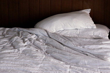 Messy bed. White pillow with blanket on bed unmade. 