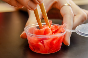 One hand with ginger and chopsticks, and the other hand holding a jar close-up on a black background