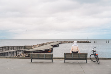 A young Caucasian woman sits with her back on a wooden bench overlooking the Baltic Sea on the...