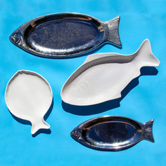 Empty fish-shaped silver and white plates on blue background. Minimal style pattern. Flat lay