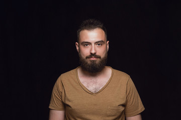 Fototapeta premium Close up portrait of young caucasian man isolated on black studio background. Photoshot of real emotions of male model. Standing and looks serious. Facial expression, human nature and emotions concept