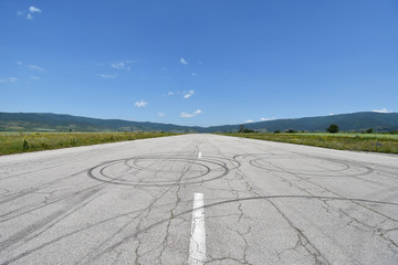 Deserted military airport runway near Sapareva Banya, Bulgaria, nowadays used for amateur car races, cracks and tire tracks seen on the old asphalt surface