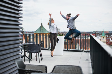 Two young business people standing on a terrace outside office, expressing excitement.