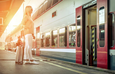 Blonde woman with her luggage stay near the red train on the per